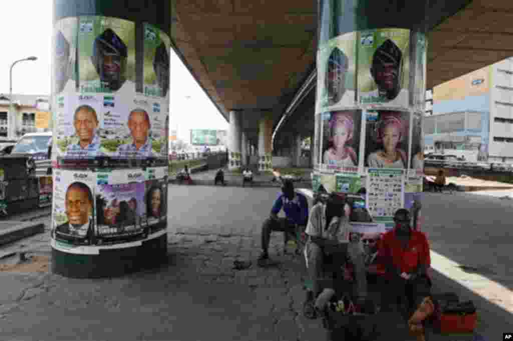 Men take a rest under a bridge pasted with election posters in Lagos, Nigeria, March 30, 2011