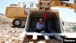FILE - A man holding a Palestinian flag protests as he sits in the scoop of an Israeli excavator as tries to prevent it from clearing his land during a protest against Jewish settlements, near the village of Deir Qaddis near the West Bank city of Ramallah, July 13, 2016.