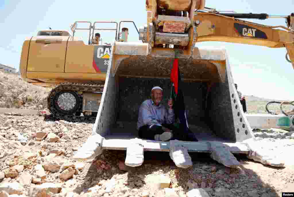 A man holding a Palestinian flag protests as he sits in the scoop of an Israeli excavator to prevent it from clearing his land near the village of Deir Qaddis near the West Bank city of Ramallah.