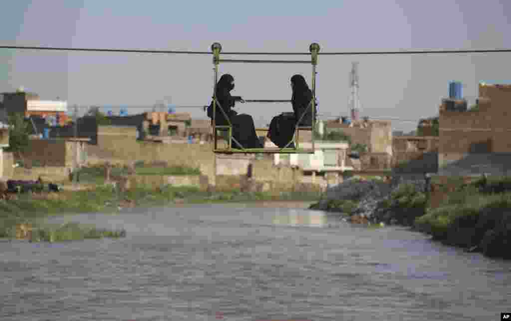 Perempuan Pakistan duduk di sebuah kereta gantung yang membawa mereka menyeberangi banjir akibat hujan deras di Rawalpindi, Pakistan.