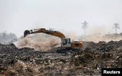 A municipal worker drives a shovel machine to extinguish a fire inside the garbage at a rubbish dump in Baghdad, Iraq, May 30, 2019.