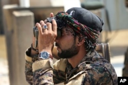 FILE - Abdullah, an Arab fighter with U.S.-backed Syrian Democratic Forces (SDF), looks through his binocular to an airstrike that hit an Islamic state militant group position, in Raqqa, northeast Syria, July 22, 2017.