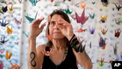 Karla Funderburk, seniman dan pemilik Matter Studio Gallery, di Los Angeles, AS, menata salah satu dari ribuan origami yang digantungnya dalam pameran yang digelar untuk menghormati para korban Covid-19, Selasa, 11 Agustus 2020. (Foto: dok).
