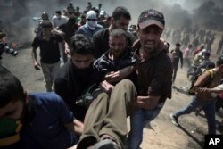 Palestinian protesters carry an injured man who was shot by Israeli troops during a protest at the Gaza Strip's border with Israel, May 14, 2018.