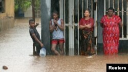 Residents stand outside a flooded house as rain falls in the aftermath of Cyclone Kenneth in Pemba, Mozambique, Apr. 28, 2019.