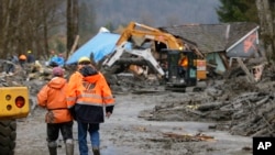 Para pekerja berjalan melewati lumpur, saat operator alat-alat berat membersihkan reruntuhan akibat musibah tanah longsor yang menghalangi jalan besar di negara bagian Washington (25/3).