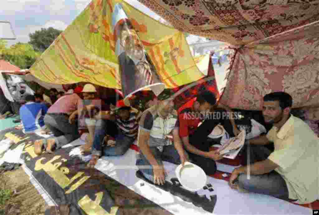 Egyptian supporters of Egypt&#39;s Islamist President Mohammed Morsi read newspapers under his poster at their camp outside of the Rabia el-Adawiya mosque near the presidential palace, July 2, 2013.