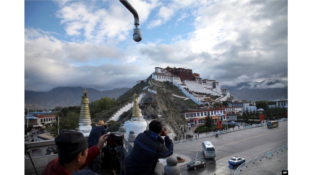FILE - In this Sept. 19, 2015, photo, tourists take photos of the Potala Palace beneath a security camera in Lhasa, capital of the Tibet Autonomous Region of China.