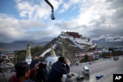 FILE - In this Sept. 19, 2015, photo, tourists take photos of the Potala Palace beneath a security camera in Lhasa, capital of the Tibet Autonomous Region of China.