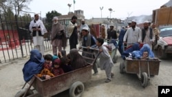 FILE - Afghan women and children sit in a cart pushed by a man as they enter Afghanistan through Pakistan's border crossing in Torkham, east of Kabul, Afghanistan, March. 11, 2015.