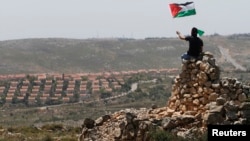 A protester waves a Palestinian flag in front of the Jewish settlement of Ofra during clashes near the West Bank village of Deir Jarir near Ramallah, April. 26, 2013.