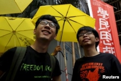 FILE - Student leaders Joshua Wong (R) and Nathan Law smile in front of supporters holding yellow umbrellas, symbol of the Occupy Central movement, outside a police station in Hong Kong, July 14, 2015.