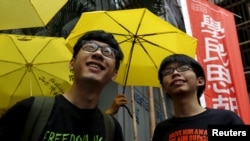 Pemimpin mahasiswa Hong Kong, Joshua Wong (kanan) dan Nathan Law di depan para pendukung yang memegang payung kuning, simbol gerakan Occupy Central movement, di luar kantor polisi di Hong Kong, 14 Juli 2015.