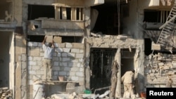 FILE - A man rebuilds a wall of a damaged building in the rebel held al-Katerji district in Aleppo, Syria, Aug. 13, 2016.