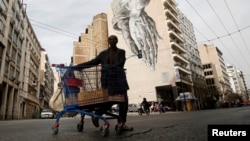 FILE - An immigrant living in Greece pushes a shopping trolley with scrap in front of a building covered with street art in Athens.