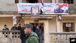 FILE - A Syrian police officer walks past a group of local people standing at a building with a portrait of Syrian President Bashar al-Assad in Salma, Syria, Jan. 22, 2016. 