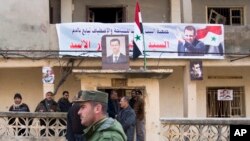 Un policier syrien passe devant un groupe de personnes arborant un portrait du président syrien Bachar al-Assad à Salma, en Syrie, le 22 janvier 2016.