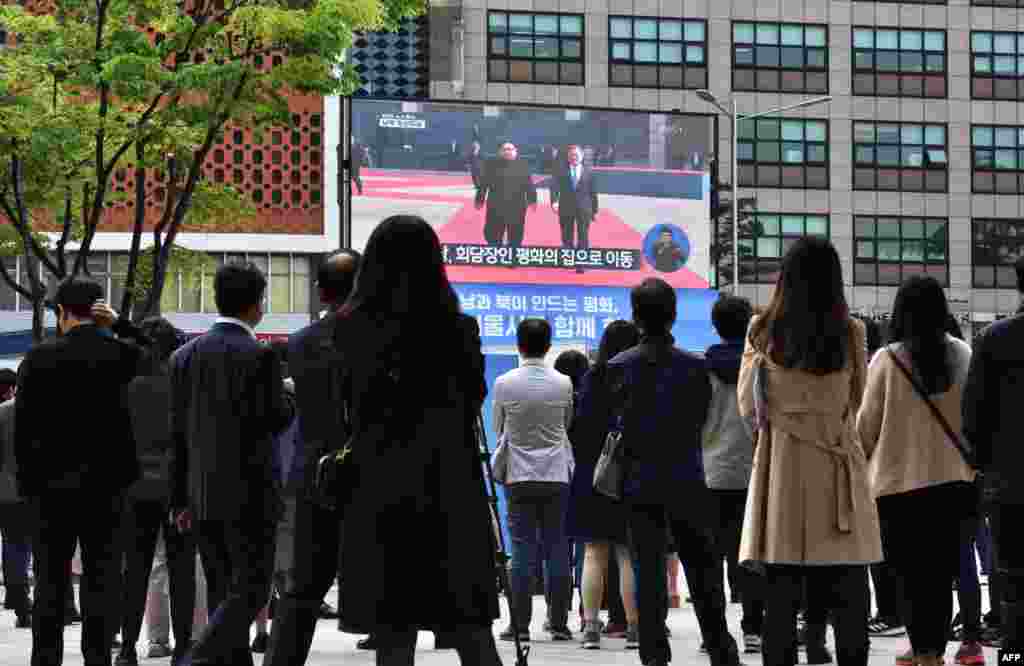 Des gens regardent en direct le président sud-coréen Moon Jae-in&nbsp; en train de marcher avec le dirigeant nord-coréen Kim Jong Un dans la zone démilitarisée, sur un écran à Séoul le 27 avril 2018.