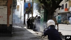 A police officer fires tear gas at close range directly into a group of anti-government protesters sheltering behind a kiosk, on a central boulevard in Dakar, Senegal, February18, 2012.