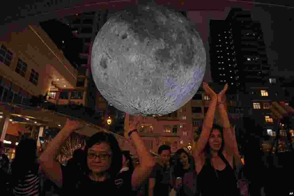 Visitors pose for photographs in front of an installation &quot;Museum of the Moon&quot;, a giant seven-meter-wide glowing sculpture of the moon, created by British artist Luke Jerram in Hong Kong to celebrate the Mid-Autumn Festival.