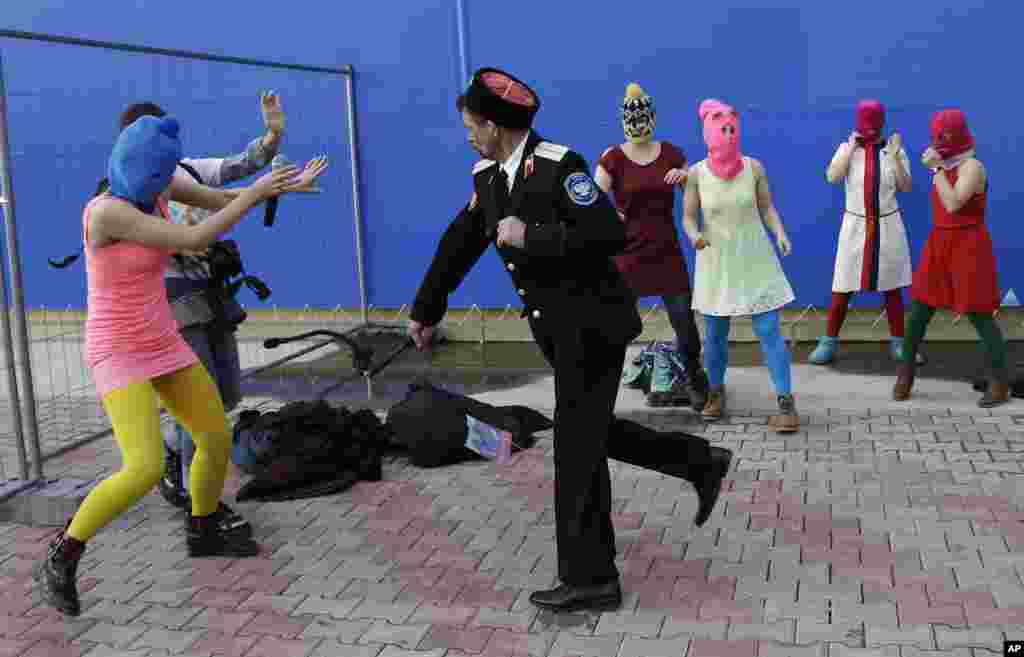 A Cossack militiaman acts out an attack against Nadezhda Tolokonnikova and a photographer in a staged protest performance with fellow members of the punk group Pussy Riot, including Maria Alekhina (center) in the pink balaclava, Russia, Feb. 19, 2014.