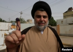 FILE - Iraqi Shi'ite cleric Moqtada al-Sadr shows his ink-stained finger after casting his vote at a polling station during the parliamentary election in Najaf, Iraq, May 12, 2018.