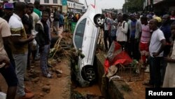People look at a car in a sewer after a flood in Abidjan, Ivory Coast, June 19, 2018. 