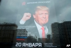 FILE - The U.S. Embassy building is reflected in a window of a Russian military outerwear shop "Armia Rossii" (Russian Army) displaying a poster of U.S. President Donald Trump, in downtown Moscow, Russia, Jan. 20, 2017.
