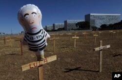 A doll representing Brazil's President Luiz Inacio Lula da Silva wearing prison clothes stands on a cross with his name in Brasilia, Brazil, Sunday, Aug. 27, 2017. Demonstrators placed crosses representing the death of corrupt politicians.