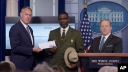 Interior Secretary Ryan Zinke, left, and Harpers Ferry National Historic Park Superintendent Tyrone Brandyburg, accompanied by White House press secretary Sean Spicer, hold up a check during the daily briefing at the White House in Washington, April 3, 2017.