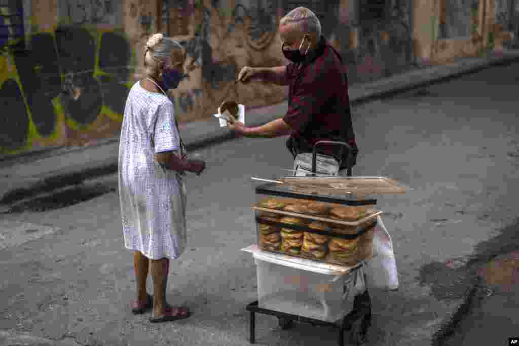 Wearing masks as a precaution against the spread of the new coronavirus, a vendor gives a complimentary, homemade guava pastry to an elderly woman in Havana, Cuba, Friday, March 19, 2021. (AP Photo/Ramon Espinosa)
