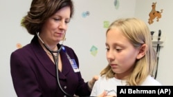 In this Tuesday, November 1, 2011 photo, Dr. Elaine Urbina, left, examines Joscelyn Benninghoff, 10, at Children's Hospital in Cincinnati. Benninghoff is taking medication to control her cholesterol.