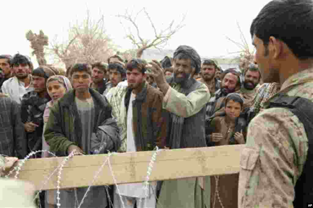 An Afghan soldier speaks to civilians gathered outside a military base in Panjwai, Kandahar province south of Kabul, Afghanistan, Sunday, March 11, 2012. Afghan President Hamid Karzai says a U.S. service member has killed more than a dozen people in a sho
