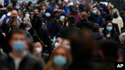 FILE - Shoppers wearing face coverings walk down Oxford Street, Europe's busiest shopping street, in London, Dec. 23, 2021. Scientists are seeing signals that COVID-19′s omicron wave may have peaked in Britain.