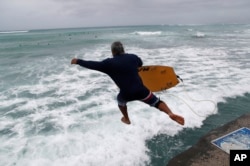 A bodyboarder jumps into the surf along Waikiki Beach ahead of Hurricane Lane, Aug. 24, 2018, in Honolulu.