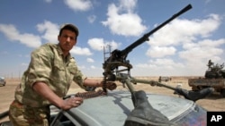 A rebel lashes a high-caliber machine gun, fitted with boots, to the roof of a car with a shoelace at a checkpoint, west of Ajdabiyah, March 31, 2011