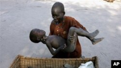 A mother gently places her son in a basket as she takes him to a medical clinic after he became infected with malaria, in Lankien, Southern Sudan.