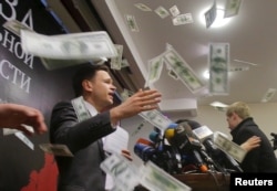 An unidentified person throws pieces of paper, resembling banknotes, as Russian opposition figure Ilya Yashin (L) presents his report in Moscow, Feb. 23, 2016.