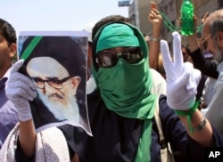 FILE - In this photo, obtained by the AP outside Iran, a female supporter of the Iranian opposition leader Mir Hossein Mousavi flashes a victory sign as she wears a green head scarf, a symbolic color of Mousavi's supporters, while she holds a poster of a leader of Iran's 1979 Islamic Revolution Ayatollah Mahmoud Taleghani, during a Friday prayer in Tehran, Iran, July 17, 2009.