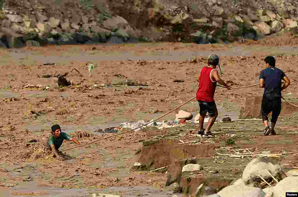 Warga berusaha menyeberangi sungai Rimac ketika banjir melanda distrik Huachipa, Lima, Peru.