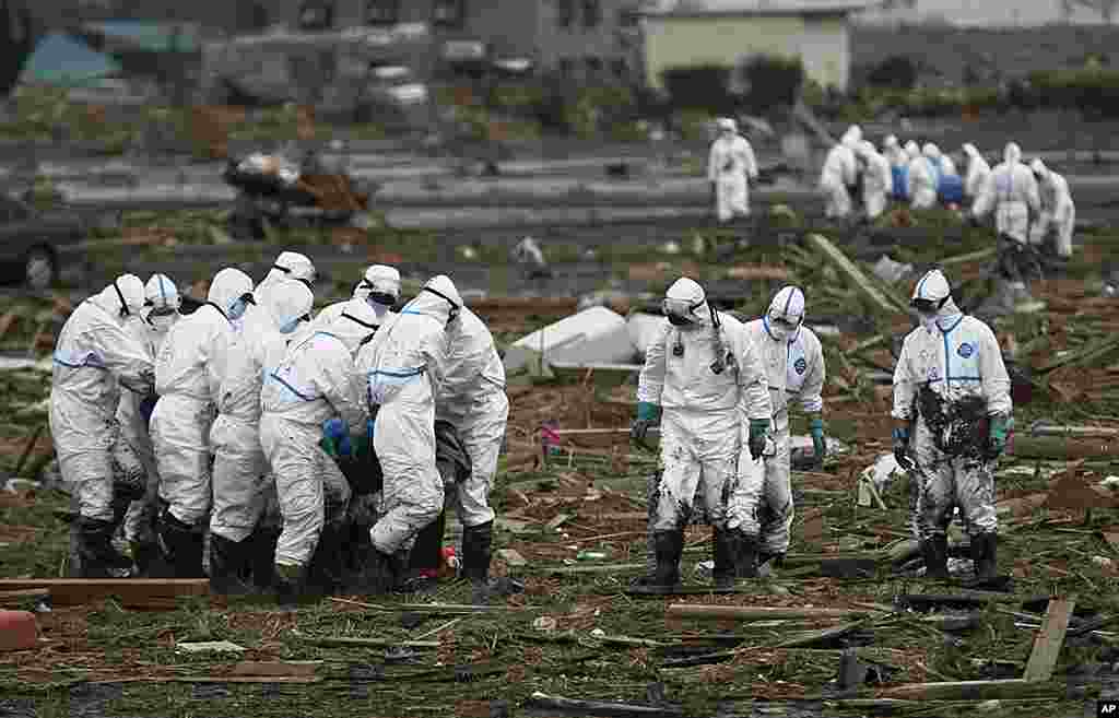 Japanese police officers wearing suits to protect them from radiation carries a victim as another group carries another body while searching for missing people in Minami Soma, Fukushima Prefecture, April 8, 2011.&nbsp;