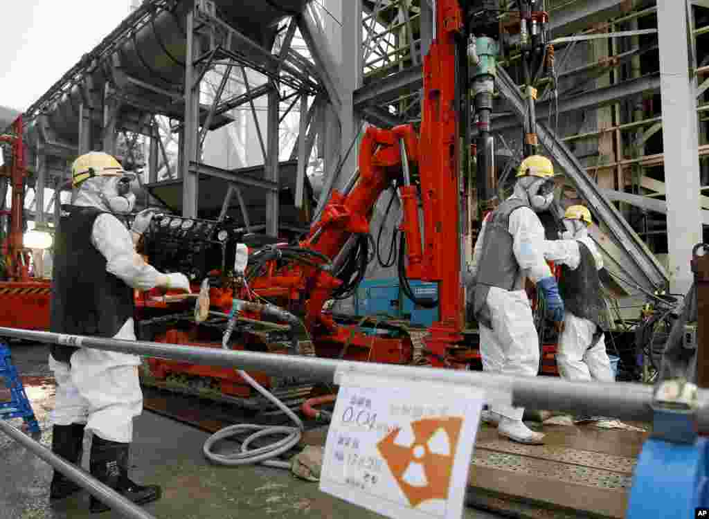 Para pekerja membor pipa ke dalam tanah yang digunakan untuk menciptakan dinding beku bawah tanah yang mengelilingi gedung-gedung reaktor yang lumpuh di pembangkit listrik tenaga nuklir TEPCO di Okuma, prefektur Fukushima, Jepang timur laut, Juli 2014. (AP/Kimimasa Mayama, Pool)