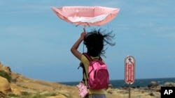 Seorang anak perempuan berusaha mengendalikan payungnya saat topan Matmo mendekati kawasan pantai di Keelung, Taiwan (22/7). (AP/Wally Santana)