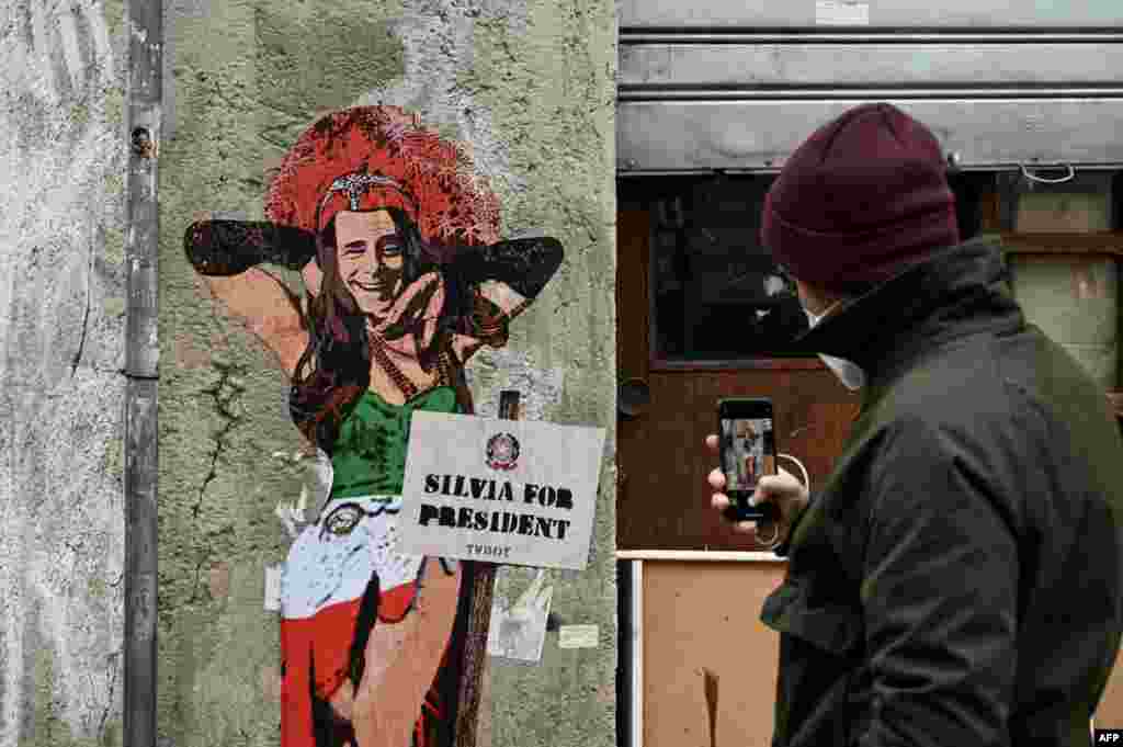 A man takes a photo of a mural entitled &quot;Thank goodness Silvia is here,&quot; representing former Italian prime minister and presidential candidate Silvio Berlusconi dressed as a woman, by Italian street artist Salvatore Benintende aka TvBoy, in Milan. 