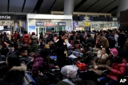 A train station worker uses a speaker phone to alert Chinese travelers to board their trains at the south train station in Beijing, Jan. 31, 2016.