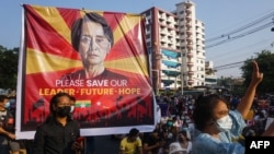 រូប​ឯកសារ៖ បដា​មាន​រូប​អ្នកស្រី Aung San Suu Kyi ​នៅ​ក្នុង​អំឡុង​បាតុកម្ម​មួយ​​នៅ​​មុខ​ការិយាល័យ​​គណបក្ស​សម្ព័ន្ធភាព​ជាតិ​ដើម្បីលទ្ធិ​ប្រជាធិបតេយ្យ​​នៅ​ទី​ក្រុង​រ៉ង់ហ្គូន​ប្រទេស​មីយ៉ាន់ម៉ា​កាល​ពី​ថ្ងៃ​ទី​១៥ ខែ​កុម្ភៈ ឆ្នាំ​២០២១។