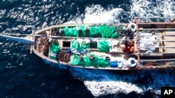 In this Dec. 20, 2021, photo released by the US Navy, service members from patrol coastal ship USS Typhoon inventory an illicit shipment of weapons while aboard a stateless fishing vessel transiting international waters in the North Arabian Sea. 