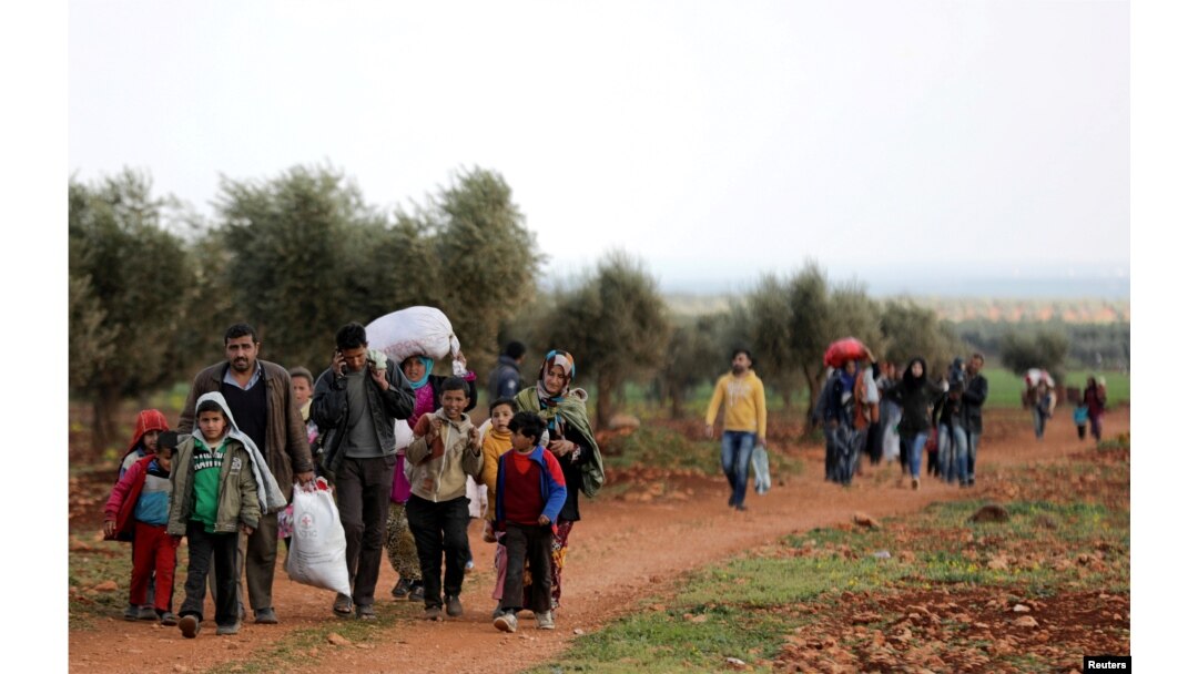 Internally displaced people walk with their belongings in the town of Inab, eastern Afrin, Syria, March 14, 2018.