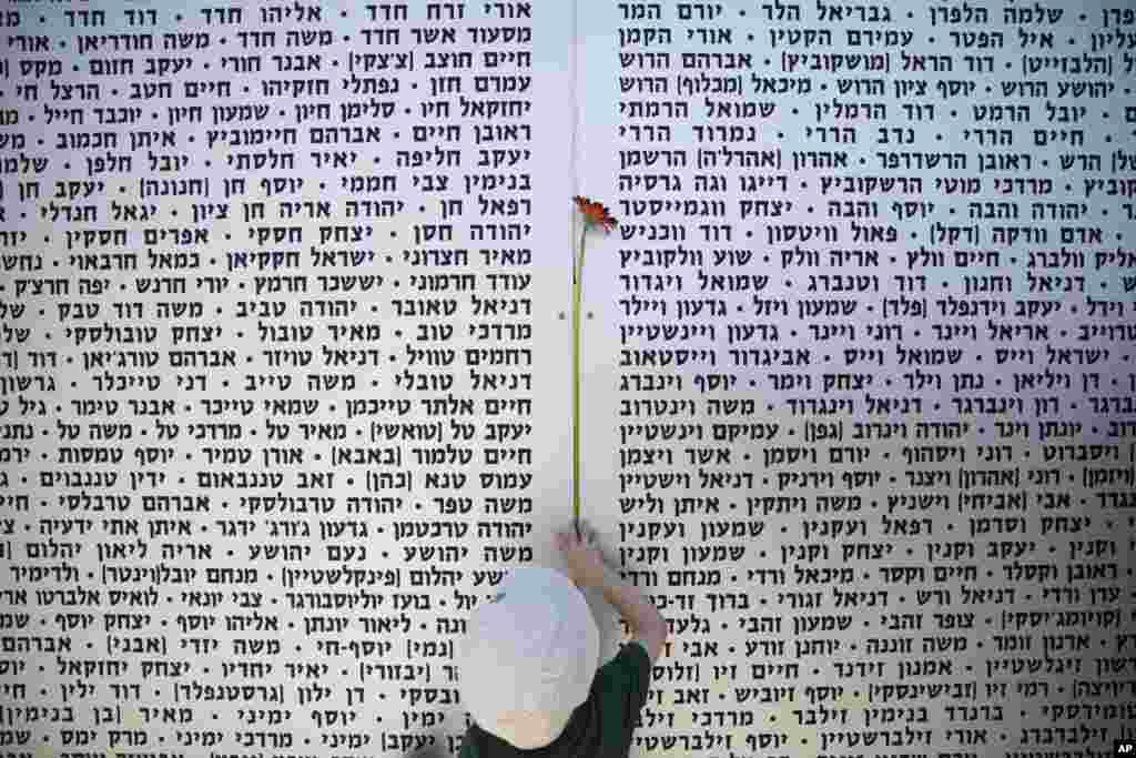 A boy hangs a flower on the wall of names of fallen soldiers following a ceremony marking the annual Memorial Day, at the Armored Corps Memorial site in Latrun, Israel.