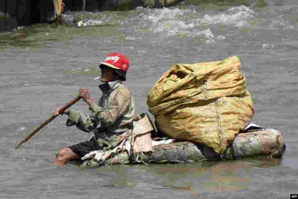 A scavenger sits on a raft as he attempts to collect recyclable materials in a river in downtown Jakarta, Indonesia.